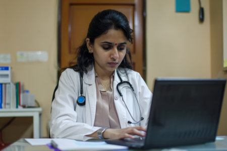 A committed Indian female therapist sits at her desk, engrossed in her laptop, meticulously preparing treatment plans and conducting research to ensure evidence-based practice and optimal patient outcomes.の素材
