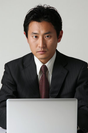 a Japanese man using a laptop, depicted in a portrait orientation on a white background. Tech-savvy individual engrossed in online activitiesの素材
