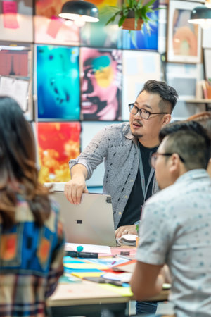 an Asian creative director leading a design meeting with team members in a colorful officeの素材