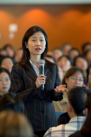 an Asian businesswoman giving a keynote speech at a corporate event with an engaged audienceの素材