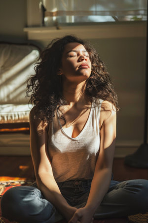 a Hispanic woman practicing deep breathing exercises in her sunlit living roomの素材