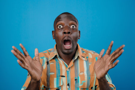 an African American man showing surprise on a blue studio backgroundの素材