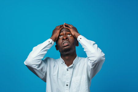 an African American man expressing anxiety on a blue studio backgroundの素材