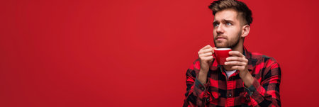 a Caucasian man in a red flannel shirt, looking thoughtful while drinking coffee on a red studio backgroundの素材