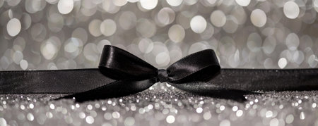 A chic black ribbon bow on a silver glitter background. The monochromatic scheme creates a modern and stylish aesthetic.の素材