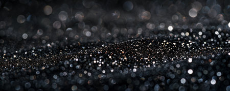 A detailed shot of black glitter with selective focus, highlighting the sharp, reflective particles in the foreground against a softly blurred, dark background, creating a dramatic effect.の素材
