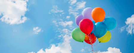A festive scene with a mix of helium balloons in bright colors, floating against a clear blue sky with fluffy clouds, symbolizing joy and festivity.の素材