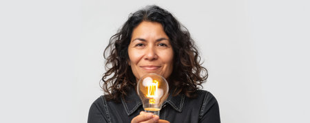 Middle-aged Hispanic woman holding a lighting bulb in hands isolated on a white studio backgroundの素材