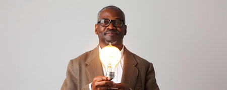 Middle-aged African American man holding a lighting bulb in hands isolated on a white studio backgroundの素材
