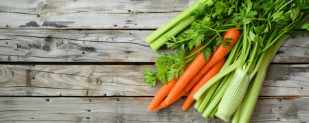 Fresh carrots, celery, and herbs arranged on distressed wooden planks. The bright colors of the vegetables contrast beautifully with the aged wood.の素材
