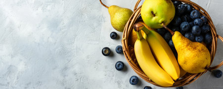 Fresh organic fruit assortment, including bananas, pears, and blueberries, in a wooden basket, top view, with plenty of space for text on a clean, white backdrop.の素材
