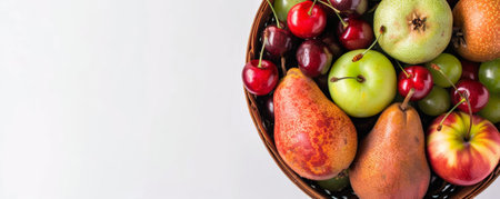 An assortment of organic fruits, including pears, cherries, and plums, neatly arranged in a wooden basket, top view, with a white background and room for text.の素材