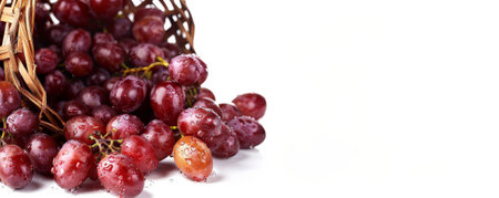 Fresh organic grapes spilling out of a wooden basket, with text space on a clean, white backdrop.の素材