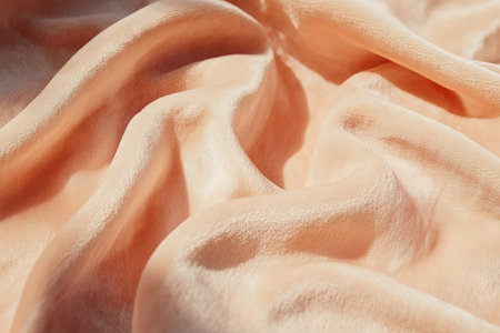Close-up of peach fuzz-hued suede leather, velvety, smooth surface with subtle shadows.の素材