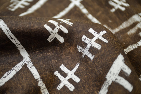 Textured African mud cloth fabric, earthy brown with white tribal symbols hand-painted onto the thick woven cotton.の素材