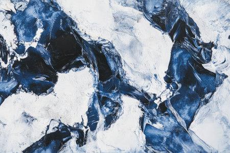 Abstract aerial view of frozen Arctic ice floes, with deep blue crevasses and pure white textures.の素材