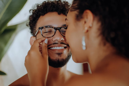 A Brazilian woman adjusting her partnerÃ¢â¬â¢s glasses, smiling as she carefully places them back on his nose.の素材