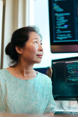 A middle-aged Asian woman reviews code snippets during a software development sprint meeting. Her technical leadership helps align back-end development with business objectives seamlesslyの素材
