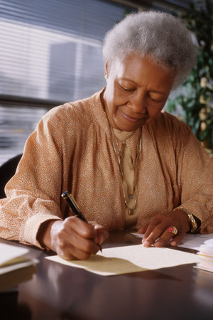 An elderly African-American woman sends handwritten thank-you notes to retirees. Her graceful tradition conveys appreciation and strong leadership values.の素材