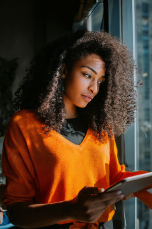 A young adult Black woman develops a digital marketing campaign while brainstorming on a touchscreen tablet. Her vibrant ideas and energy capture a fresh, modern tone for brand storytellingの素材