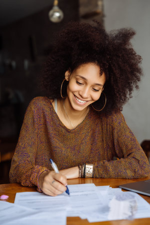 A young adult African-American woman drafts a motivational newsletter with inspirational quotes and team wins. Her optimism uplifts morale and builds community through wordsの素材