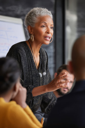 A mature Black woman leads an HR meeting on inclusivity practices in hiring. Her strong voice and inclusive values foster change from withinの素材