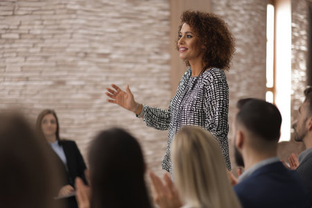 A mature Hispanic woman gives a presentation on global business etiquette, sharing insights on cultural protocols, greetings, and dress codes with an audience of international sales staffの素材