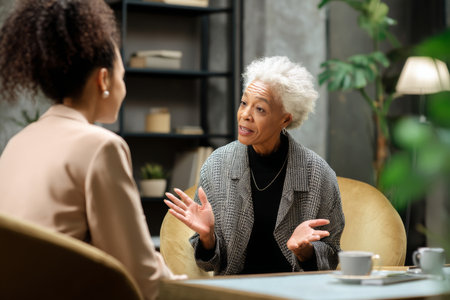 An elderly Black woman gives personal advice to a younger manager during a coffee chat, sharing stories of triumph, burnout, balance, and growing into executive leadershipの素材
