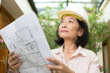 A middle-aged Asian woman compares proposal vendors for a green office renovation, evaluating quotes and certifications while visualizing improvements in energy efficiency and designの素材