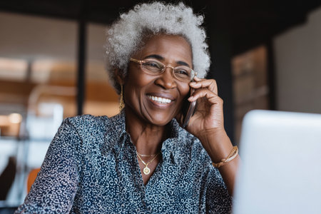 An elderly Black woman discusses logistics with an overseas colleague via speakerphone, finalizing shipment details and customs procedures.の素材