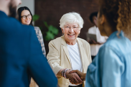 An elderly Caucasian woman welcomes new employees with a sincere smile, sharing her career story and offering guidance in an inclusive, supportive way.の素材