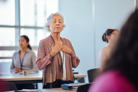 An elderly Hispanic woman leads a midday mindfulness break, helping coworkers unwind with gentle stretches and calming breathwork to support well-being at work.の素材
