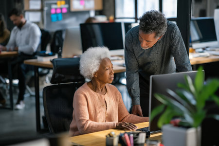 An elderly Black woman checks ergonomic seating arrangements in the workspace, consulting with a wellness coach to ensure every employee has optimal support for their health and productivityの素材