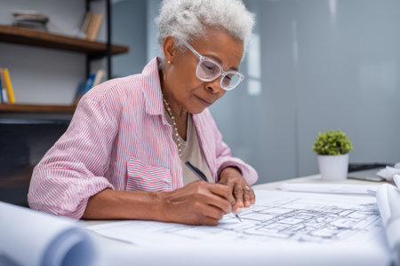 Elderly African-American woman designing a new ergonomic office layout, sketching seating arrangementsの素材