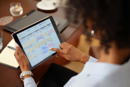 Mature Black woman scheduling international meetings, balancing time zones and appointments on a digital calendarの素材