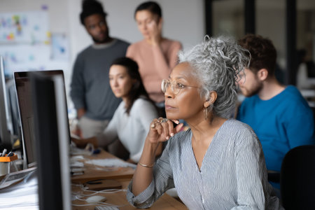 Middle-aged African-American woman reviewing tech support tickets with the IT team, discussing patterns in recent user issuesの素材
