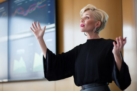 Mature Caucasian businesswoman standing in front of a conference room screen, passionately delivering a presentation about quarterly trends. Her outfit is sharp, and her confidence commands attention from the room.の素材