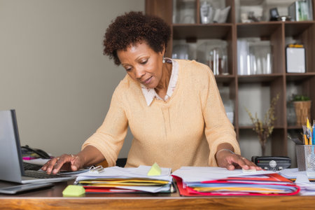 Middle-aged Black woman preparing her department for an internal audit, organizing compliance documents into digital foldersの素材