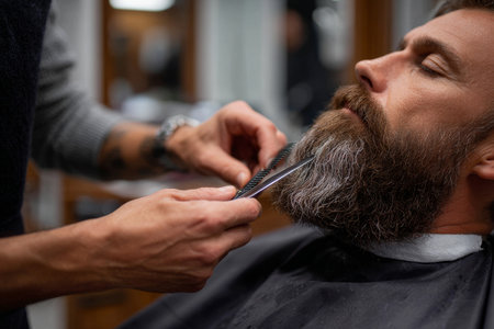 A barber carefully trims a customer's beard, capturing a moment of precision and grooming expertise.の素材