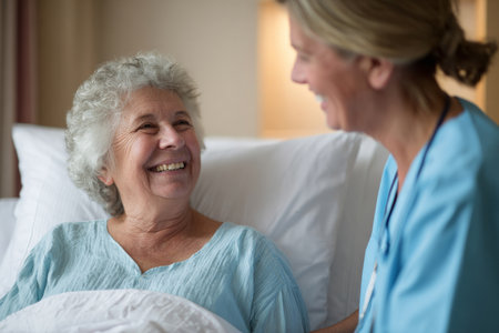 A warm and inviting image showcasing a healthcare professional in scrubs interacting with a smiling elderly woman in a hospital bed. The soft pastel colors of the room create a calming atmosphere. This scene captures a moment of care and compassion, perfect for health-related and wellness themes in stock photography.の素材