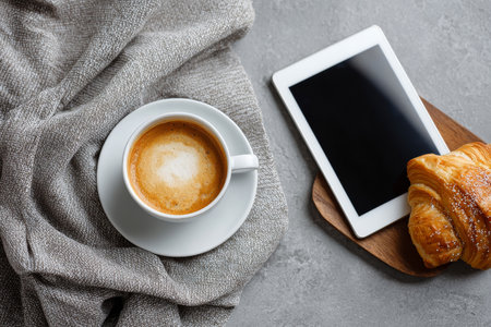 Top view of coffee with pastry and tablet with white screen on concrete surfaceの素材