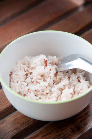 White and brown steamed rice in white round bowl and spoon on wood pattern backgroundの写真素材