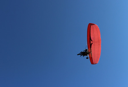 Paraglider and a passenger on a red paraglider with a motor are flying in the blue sky.の写真素材