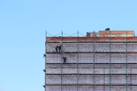 workers on the scaffolding are building nine-story house from blocks and bricks.の写真素材