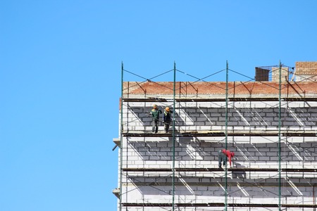 workers on the scaffolding are building nine-story house from blocks and bricks.の写真素材