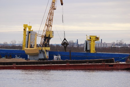 the process of loading coal from the barge to the ship on the river with the help of the port cargo craneの写真素材