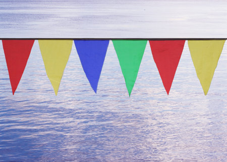 Multi Colored Triangular Flags Hanging in the Sky at an Outdoor on the background of blue waterの写真素材