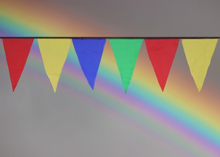 Multi Colored Triangular Flags Hanging in the Sky at an Outdoor against the backdrop of a rainbowの写真素材