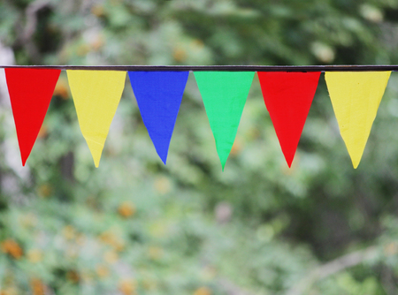 Multi Colored Triangular Flags Hanging in the Sky at an Outdoor against the backdrop of a green grass.の写真素材