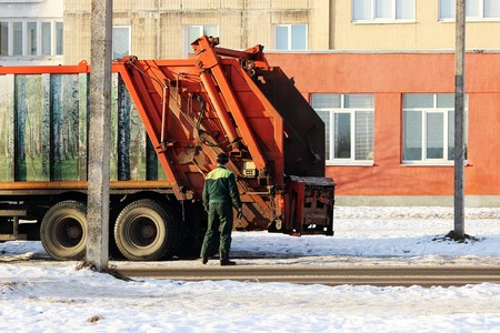 Worker standing next to a junk car after loading garbage tankの写真素材
